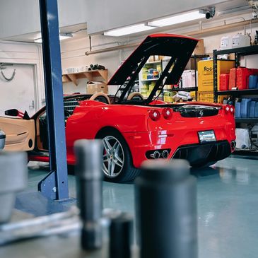 Red Ferrari with open hood and door in a garage workshop.