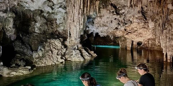 Group exploring a picturesque underground cave with clear water and stalactites.