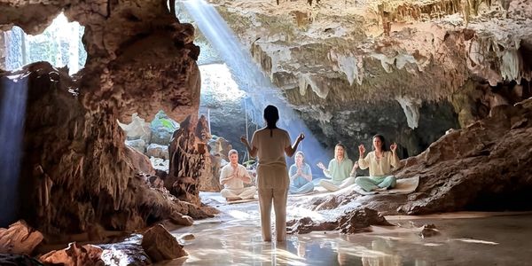 Group meditation inside a sunlit cave with natural rock formations.