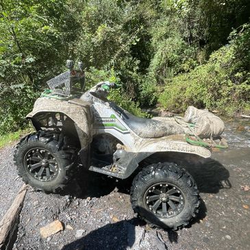 Muddy Kawasaki ATV in a forest creek.