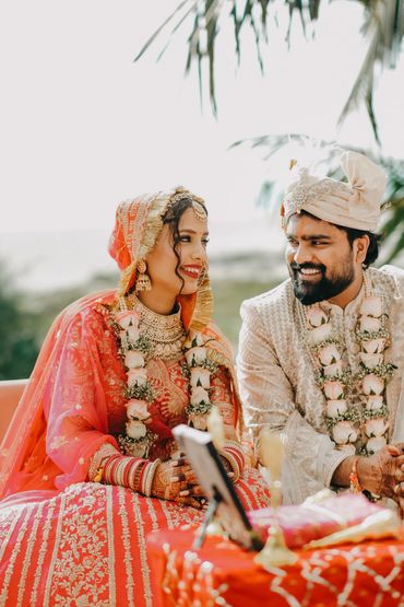 Happy Indian bride and groom in traditional wedding attire smiling at each other.