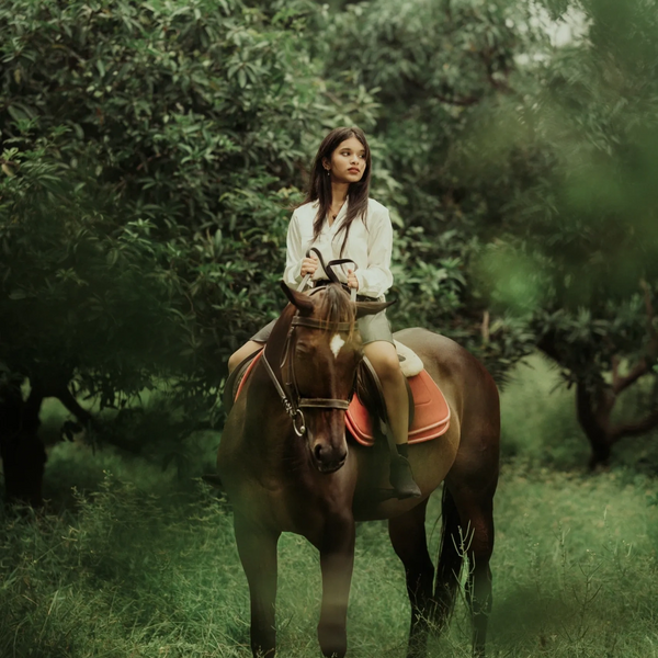Young woman riding a brown horse in a green forested area.