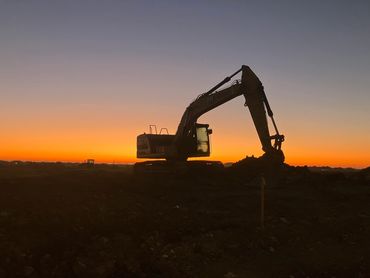 Silhouette of a CAT excavator against a vibrant sunset sky.