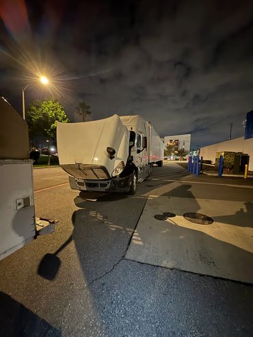 White semi-truck with open hood parked at night under streetlight.