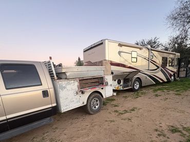 Truck with a utility bed parked next to a large motorhome at dusk.