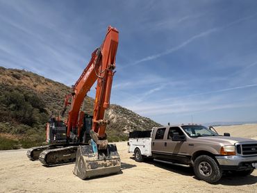 Excavator and pickup truck in a desert landscape under a clear blue sky.