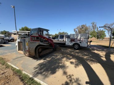 Construction equipment and vehicles parked at a work site under clear blue sky.