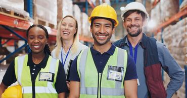 Smiling warehouse workers in safety gear pose for a group photo.