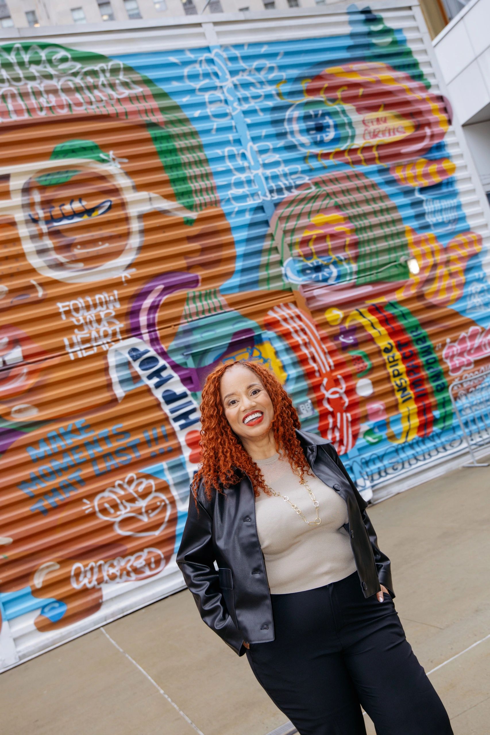 Woman smiling in front of colorful mural.