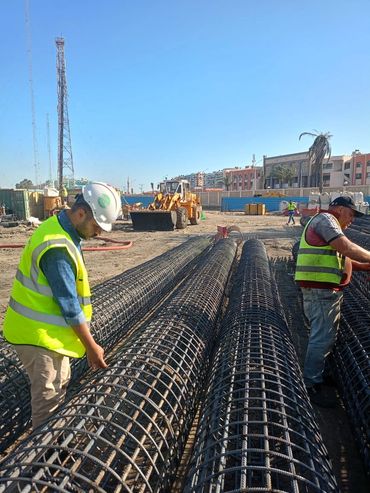 Workers inspecting steel rebar cages at construction site.