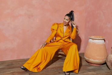 Woman in bright orange suit sitting on a chair, smiling.