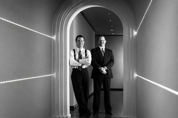 Two men in formal attire stand in an arched hallway.