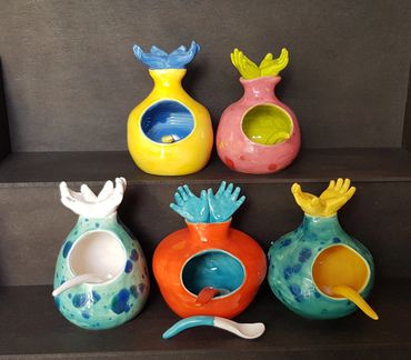 Group of colourful salt cellars with hands for handles