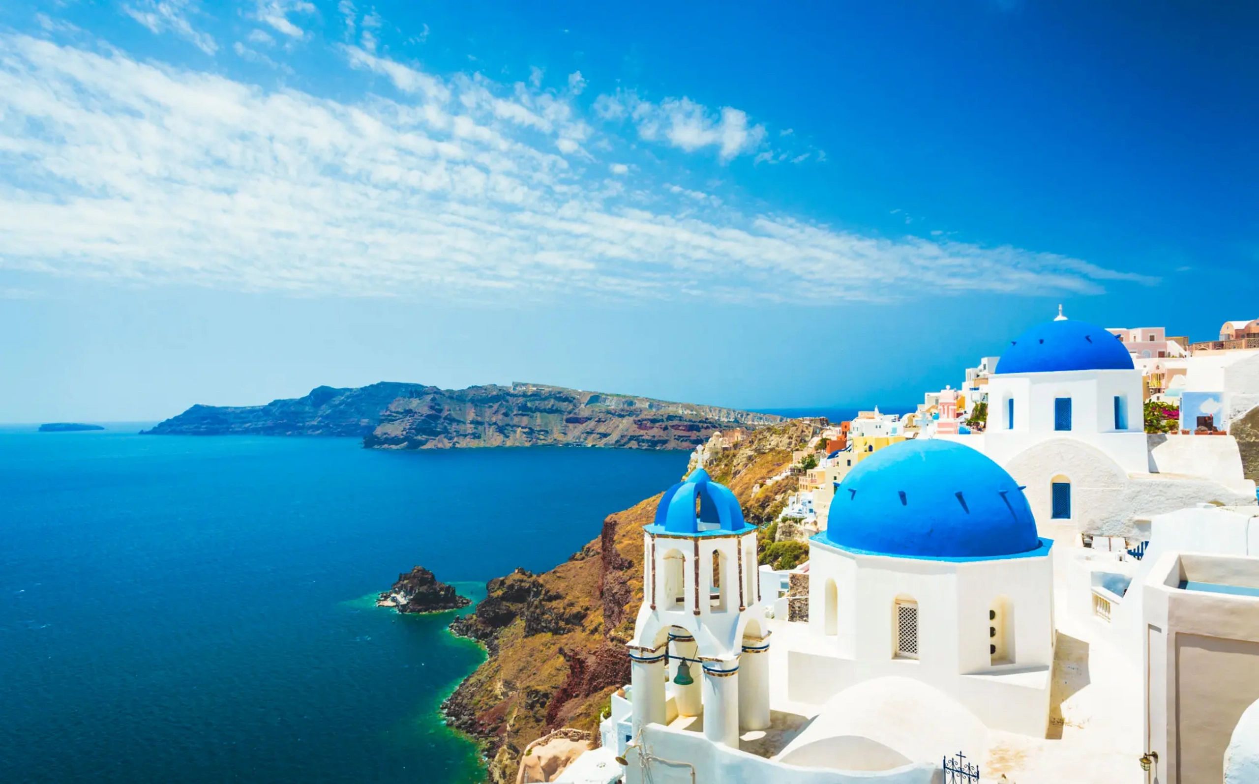 Santorini's iconic blue-domed churches overlooking the Aegean Sea under a bright sky.