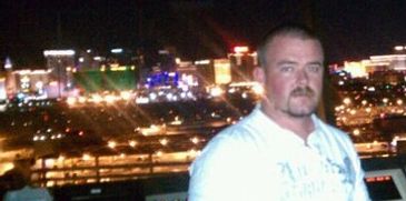 Man posing at night with city lights in the background.