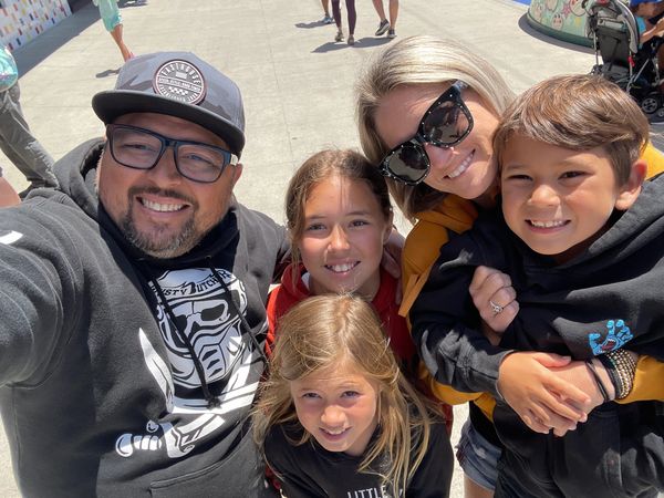 Smiling family of five enjoying a sunny day outdoors, taking a close selfie together.