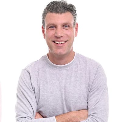 Smiling man in a light gray long-sleeve shirt with arms crossed.