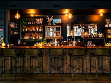 Wide view of bar interior with wooden counter, stools, and warm lighting