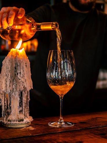 White wine poured into a glass beside a melting candle in a dim bar