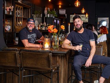 Two bar owners at the counter with drinks and warm ambient lighting