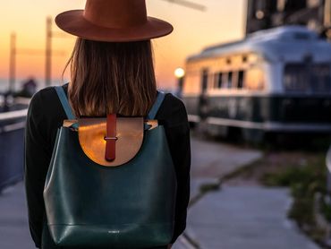 Woman wearing a leather backpack walking near a train at sunset