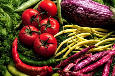 Colorful fresh vegetables with water droplets in dramatic light, including tomatoes, beans, and eggp