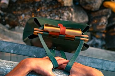 Close-up of green leather backpack and hands on railing in golden hour light