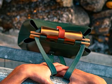Hands holding a green leather bag with gold and red strap details outdoors
