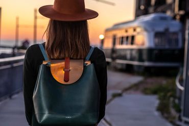 Back view of woman wearing leather backpack at sunset with vintage tram in the background