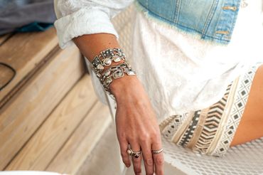 Boho bracelets and rings on woman’s hand wearing white lace and denim vest