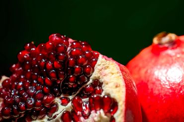 Close-up of a ripe pomegranate with glistening red seeds and dark green background