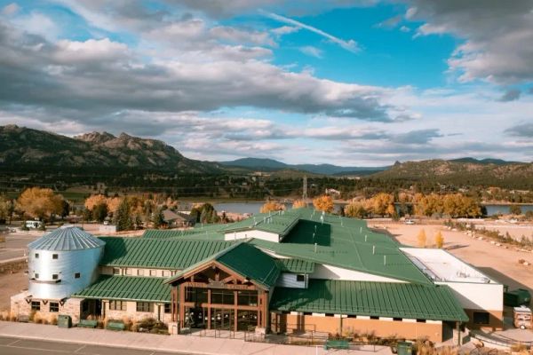 Large building with green roofs set against a mountainous backdrop under a partly cloudy sky.