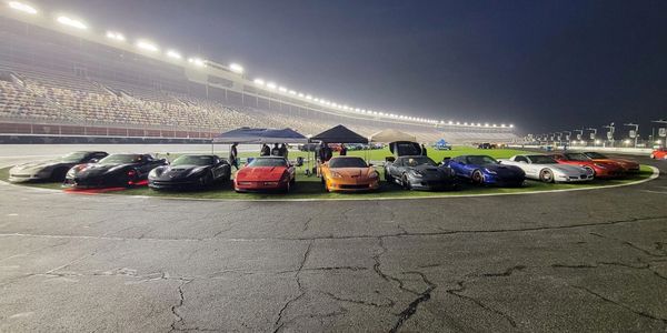 Cars lined up on a racetrack under the lights. 
