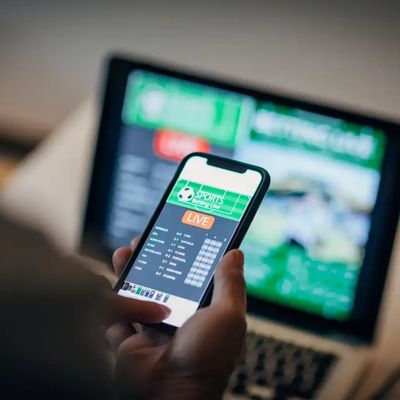 betting bet sports phone gambling laptop over shoulder football live home website concept