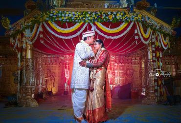 A couple in traditional attire shares a tender moment under vibrant floral decorations.