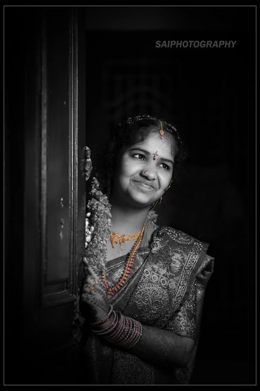 Smiling woman in traditional attire peeks from behind a door, highlighted with selective color on jewelry.