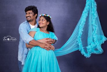 Couple embracing with smiles, woman in blue dress and floral crown.