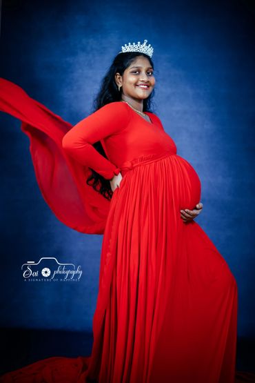Pregnant woman in a flowing red dress and crown, smiling confidently.