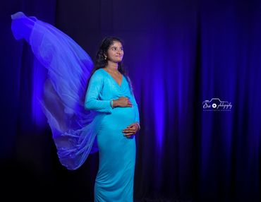 Pregnant woman in blue dress with flowing fabric against a dark blue background.