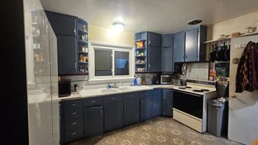 Cozy kitchen with blue cabinets, white countertops, and hanging pans near the stove.