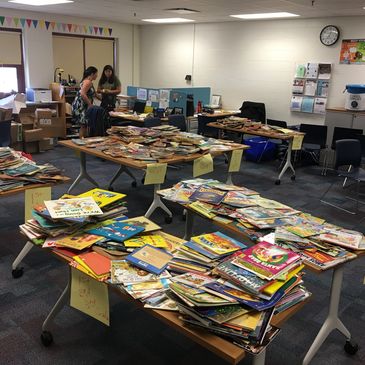 Tables full of books sorted by labels in a room with two people.