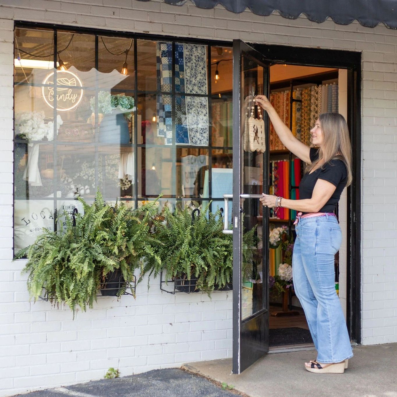 A woman opens the door to a quilt and craft shop named Whistlestop Makers Market.