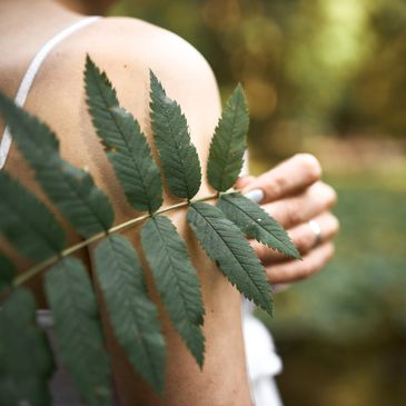 Women pictured from behind holding a forest leaf against her shoulder