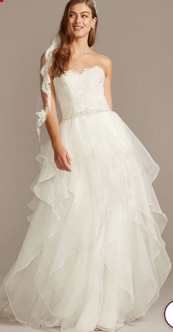 A smiling bride in a strapless layered wedding gown with a lace veil.