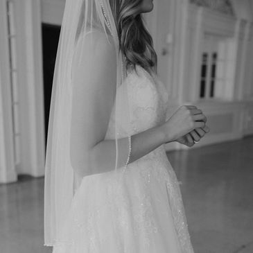 Bride in lace wedding dress and veil, hands gently clasped.