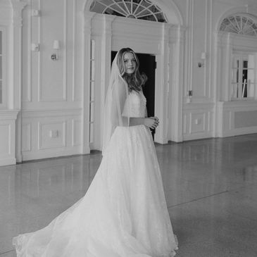 Bride in a flowing wedding dress standing in an elegant room with chandeliers.
