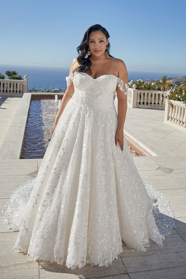 Curvy woman in a beautiful off-shoulder white lace wedding dress outdoors.