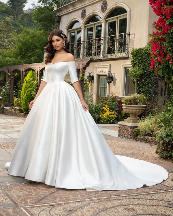 Bride in elegant off-shoulder white wedding gown with long train outdoors.
