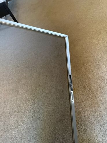 Close-up of a window screen frame on carpeted floor.
