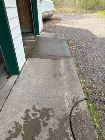 Wet concrete sidewalk next to a garage with a hose on the ground.
